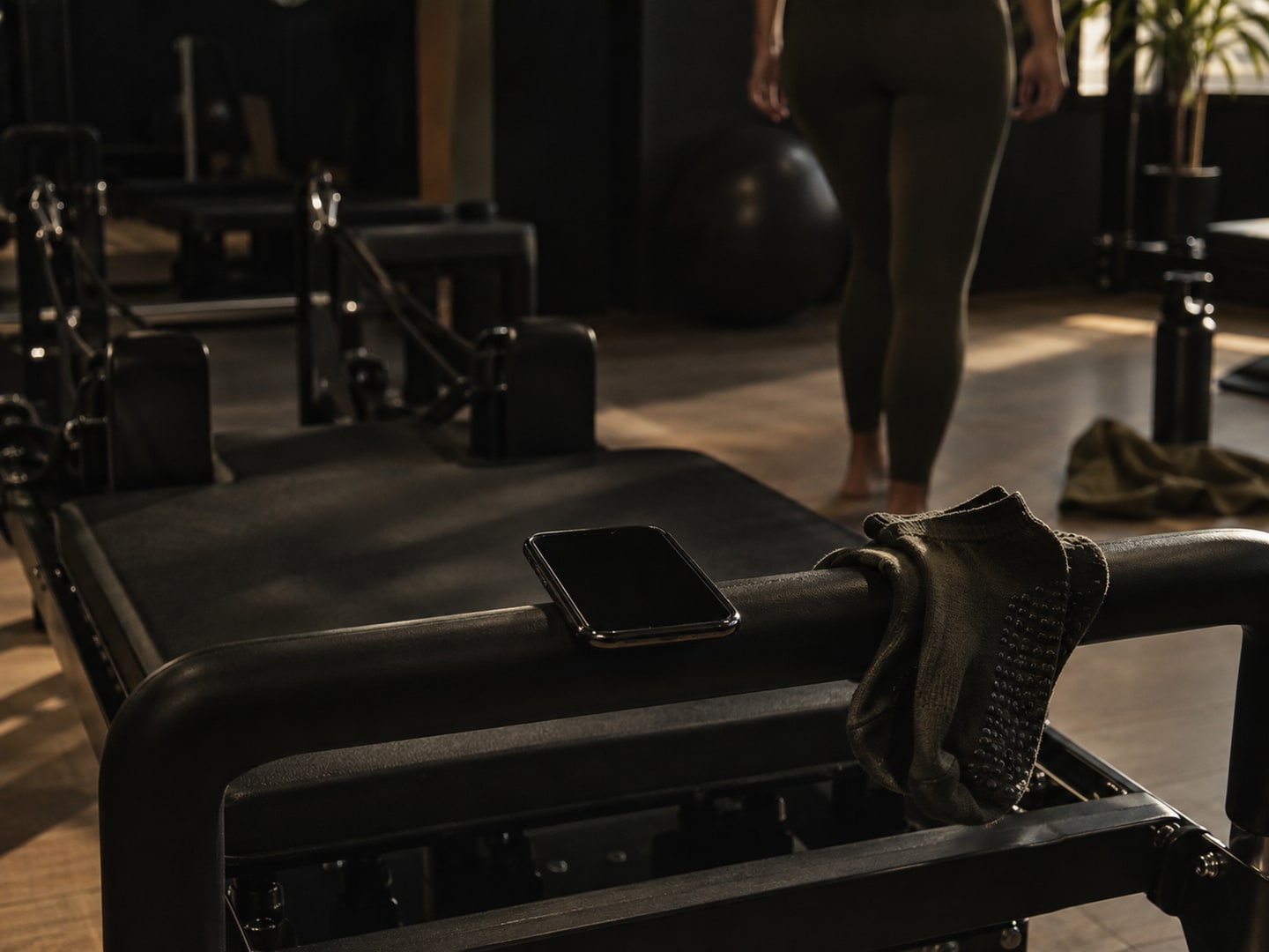 A phone lying on the footbar of a reformer, grip socks hanging beside it.